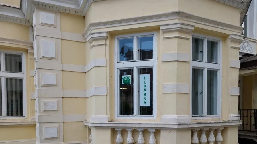 Historická budova s arkýřovým oknem, kde sídlí lékárna, viditelná informační cedule s logem lékárny.